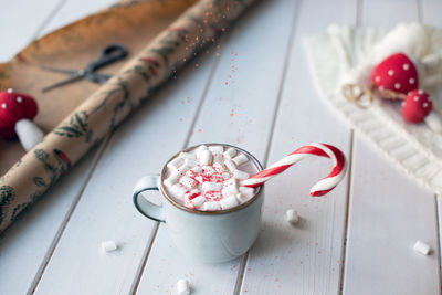 Christmas cocoa with candy cane, marshmellow and falling red sugar on white wooden background