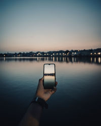 Hand holding smart phone against sky during sunset