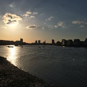 Scenic view of river by buildings against sky during sunset in city