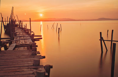 Wooden posts in sea against sky during sunset