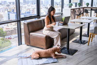 Side view of woman with dog sitting on sofa at home