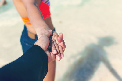 Cropped image of boyfriend holding girlfriend hand at beach