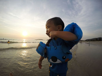 Boy wearing puddle jumper at beach against sky during sunset