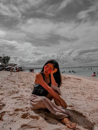 Woman wearing sunglasses while sitting on beach against sky