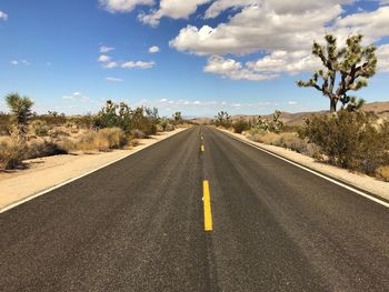 Empty road by trees against sky