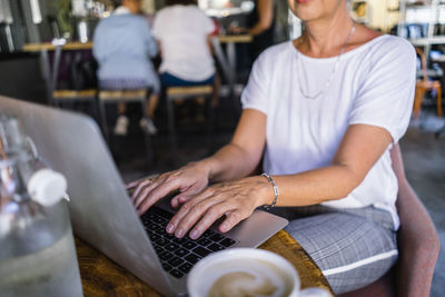 Midsection of woman using laptop on table in cafe