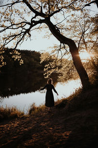 Rear view of woman standing by tree against sky during sunset