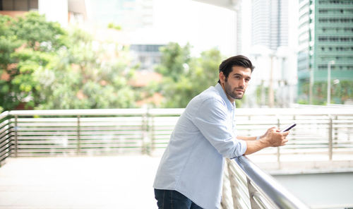 A young caucasian man using a smartphone and smiling while waiting for his friend at the outside.