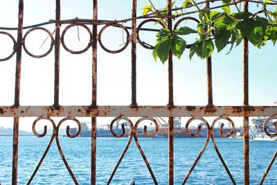 Metal railing by sea against sky