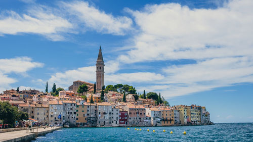 Buildings at waterfront against cloudy sky