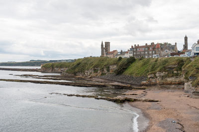 Buildings by sea against cloudy sky