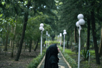 Side view of woman wearing hijab standing on footpath in park
