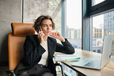 Young woman using mobile phone while sitting in office