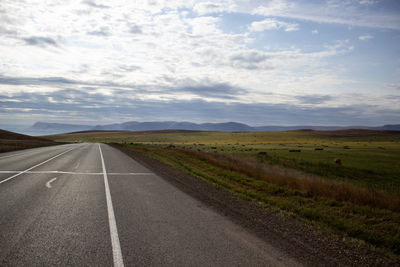 Road passing through field against sky