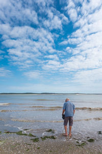 Rear view of man standing at beach against cloudy sky