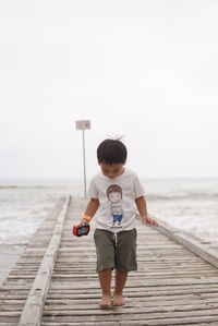 Rear view of boy on pier over sea against clear sky