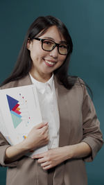 Portrait of smiling young businesswoman standing against blue background