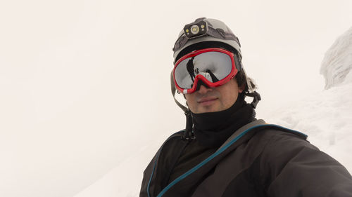 Climber with helmet and headlamp taking a selfie on a glacier on a cloudy day, reflected in glasses