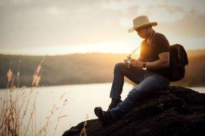 Man sitting on rock against sky during sunset