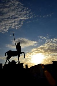 Low angle view of silhouette man statue against sky during sunset