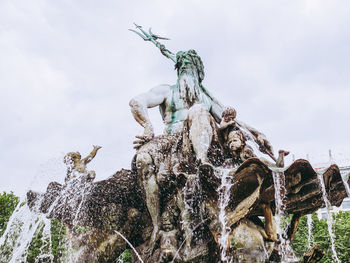 Low angle view of statue by fountain against sky