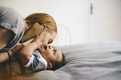 Mother kissing son while talking on mobile phone at bed