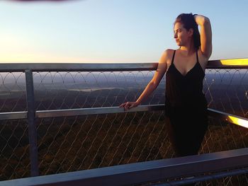 Woman standing by railing against sea against clear sky
