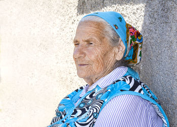 Old pensive grandmother at a kerchief on a gray background