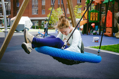 Full length of teenage girl sitting on swing at playground
