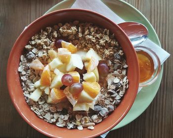 Directly above shot of breakfast cereal with fruits in bowl by honey on table