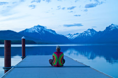 Rear view of woman sitting on pier against lake