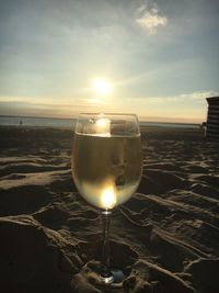 Close-up of beer glass on beach against sky during sunset