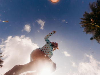 Low angle view of child jumping with arms outstretched against sky
