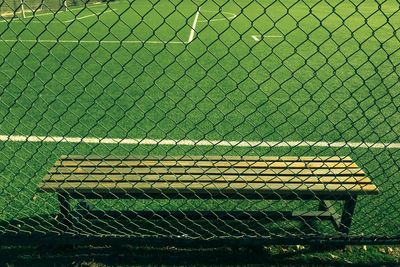 Empty bench by chainlink fence