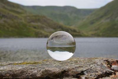 Reflection of crystal ball on rock by lake
