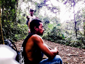 Full length of shirtless man sitting in forest