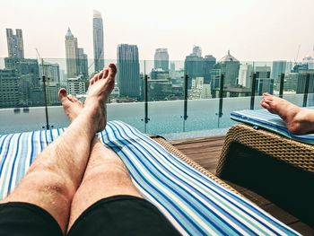 Low angle view of man relaxing at poolside against modern buildings