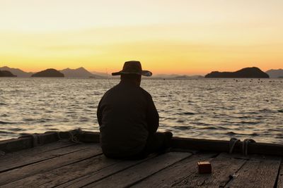 Man sitting by sea against sky during sunset