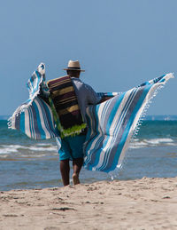 Rear view of man with sheet walking at beach against sky