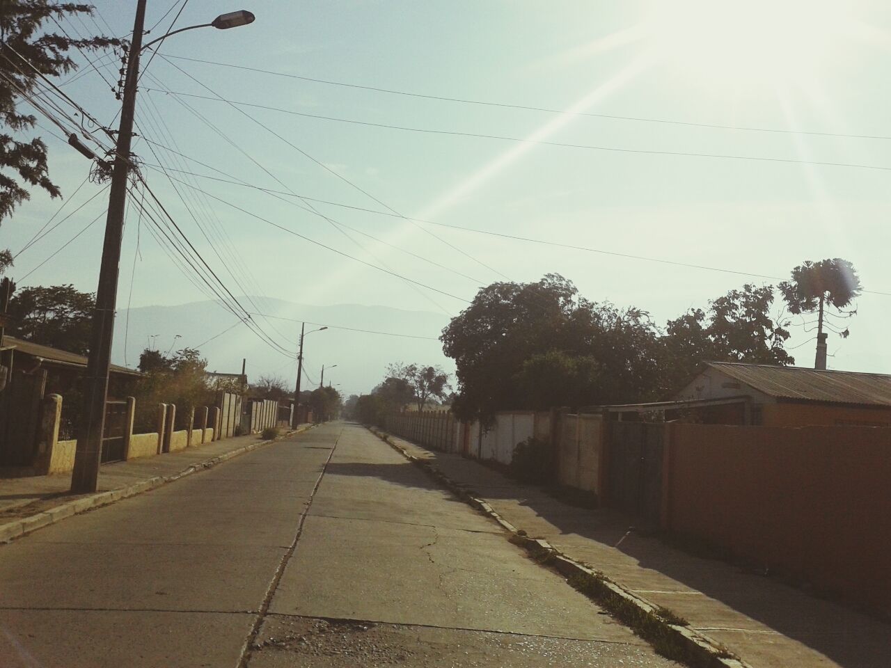 building exterior, the way forward, built structure, architecture, sky, tree, diminishing perspective, transportation, vanishing point, sunlight, street, road, power line, house, city, outdoors, empty, sun, no people, electricity pylon