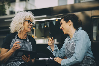 Senior owner talking to assistant against food truck in city