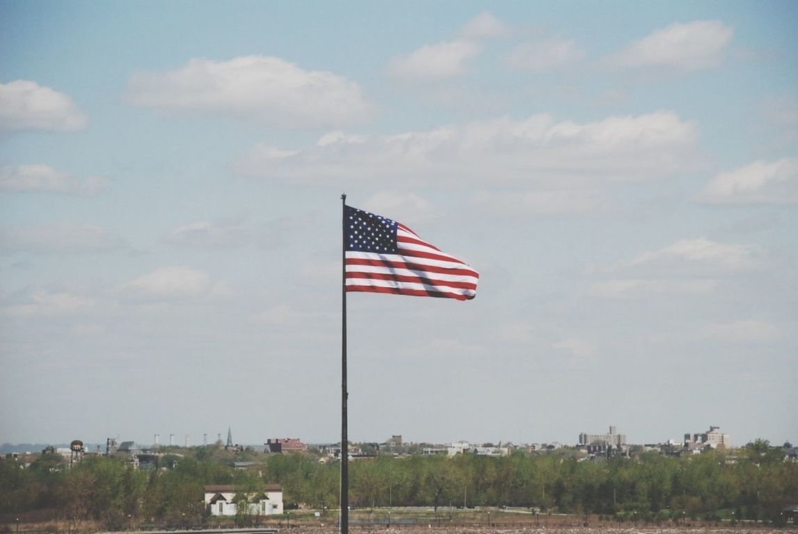 patriotism, flag, identity, national flag, american flag, sky, wind, low angle view, striped, pole, red, culture, pride, cloud - sky, cloud, building exterior, built structure, flag pole, architecture, day