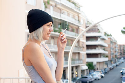 Side view of woman smoking cigarette in front of urban scene 