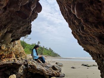 Woman sitting on rock against sky