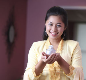 Portrait of young woman holding oil lamp while standing at home