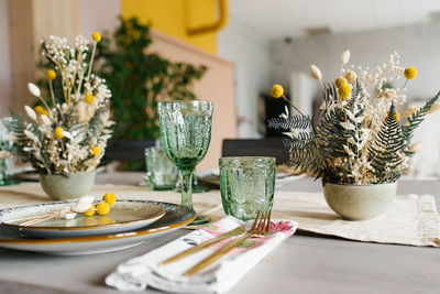 Rustic dining table setting, dried flowers in a vase, green glass glasses and ceramic plates