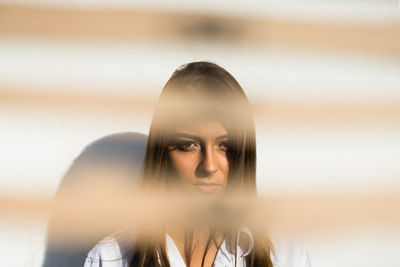 Portrait of young woman seen through window blinds