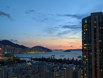 Illuminated buildings by sea against sky at sunset