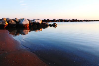 Rocks in sea against sky during sunset