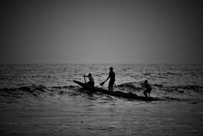 Silhouette people on sea against clear sky